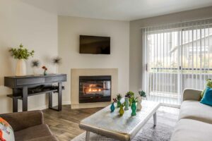 Neutral toned Living room, gas fireplace, patio sliding door, tv above fireplace, coffee table, wood toned vinyl floor