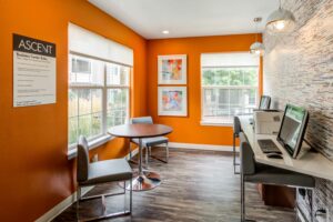 Business center, orange walls, Cafe table with 2 seats, 2 computer workstations, large bright windows, wood floor