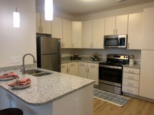 kitchen, stainless steel appliances, neutral toned wood cabinets, granite countertops, kitchen island, dual sink, refrigerator, microwave, oven,
