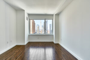 Unit Bedroom, wall to wall far side window, hardwood floors, white walls, widow view of city and sprawling skyline.