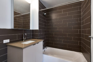 Unit Bathroom, vanity mirror with storage, sink with storage underneath, shower/bath, tile floor, dark subway tiled walls.