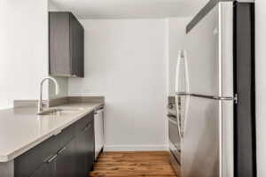 Unit Kitchen, hardwood floors, stainless steel appliances, dark brown/black cabinets and storage, white walls.