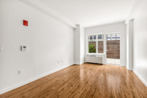 Unit Living Room, Hardwood Floors, window and door leading to patio, white walls, Furnace/AC in front of window.