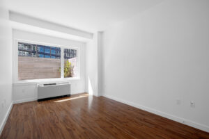 Unit Bedroom, AC/Furnace in front of window, White walls, hardwood floors wall to wall window.