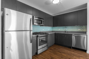 Unit Kitchen, hardwood floors, stainless steel appliances, dark brown/black storage and cabinetry, light blue subway tile between cabinets and countertops