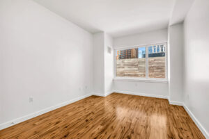 Unit Bedroom, White walls, hardwood floors, wall to wall windows, view of patio.