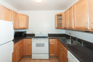 Unit Kitchen, Light brown cabinets, white appliances, wood floors, black granite countertops.