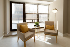 Unit Living room, 2 lounge chairs side table, floor to ceiling windows, patio door behind chairs