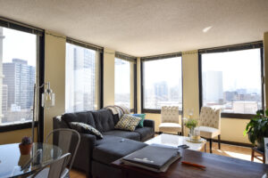 Unit Living room, circular 4-seat dining table, sectional couch, large coffee table, wood floors, large windows, view of downtown chicago.