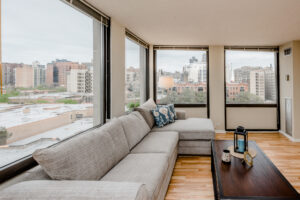 Unit Living Room, Wood Floors, Large windows along perimeter, Gray Sectional Couch, View of Downtown Chicago.