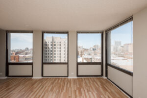 unit living room, wood floors, large windows with view of downtown chicago along perimeter.