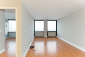 Unit Living Room, bedroom on other side of wall, wood floors, 2 large windows on outer wall.
