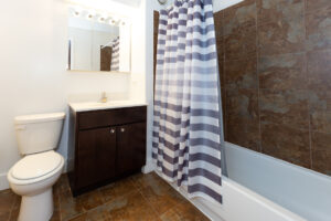 Unit Bathroom, tile floor, dark brown cabinets, well lit vanity mirror.