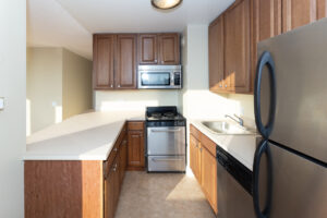 Unit Kitchen, stainless steel appliances, dark brown cabinets, tile floor.