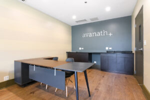 Interior Lincoln Park Plaza Leasing Office, wood floors, gray wall with silver avanath signage in back of room, office desks, built-in cabinets in background.