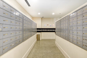 Interior Mailroom, rows of cluster mailboxes, concrete floor, tile design on the wall, security cameras.