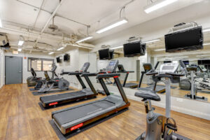Interior Lincoln Park Plaza's Fitness Center, Wood Floors, Mirrored walls, Multiple Mounted TVs, Treadmills, Stationary bikes, Ellipticals, Free-Weights.
