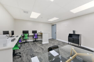 Interior business center, four computer stations, white walls, printer, glass table with four seats, coffee bar.